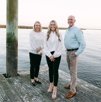 A woman and two men standing on a wooden pier next to a body of water - https://www.rhinspartners.com/